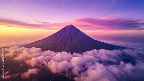 A bird's eye view of a majestic mountain peak emerging above a blanket of clouds, with the sun casting a warm glow at dawn, the sky painted in soft gradients of pink and purple photo