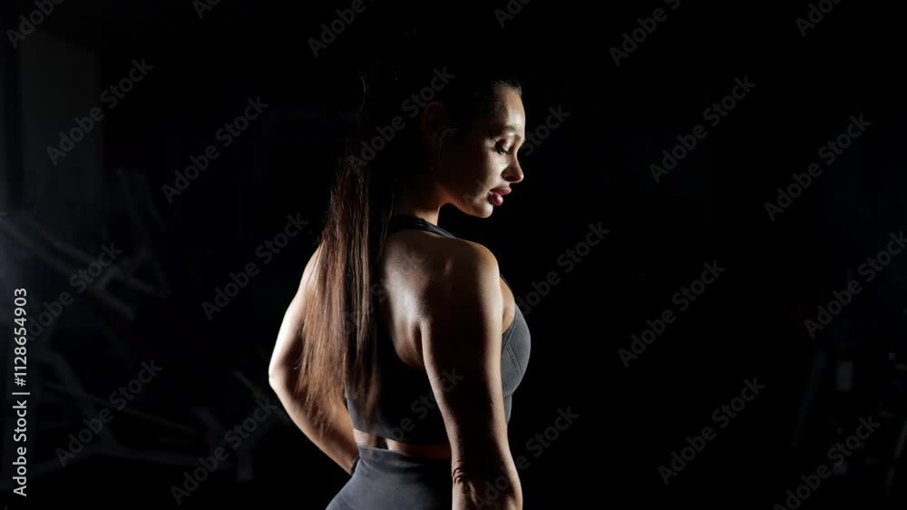 A female bodybuilder with long dark hair poses with a dark room on a black background. The silhouette of an athletic woman in sportswear. A woman shows a muscular body, an incentive to exercise. A female bodybuilder with long dark hair poses with a dark room on a black background. The silhouette of an athletic woman in sportswear. A woman shows a muscular body, an incentive to exercise.