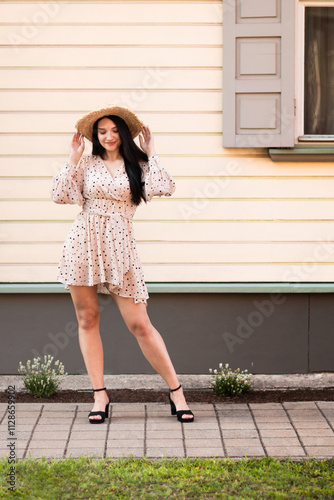 A young woman in a summer dress and hat enjoys a carefree holiday on a sunny day. A holiday feeling in a small town, by nature. 