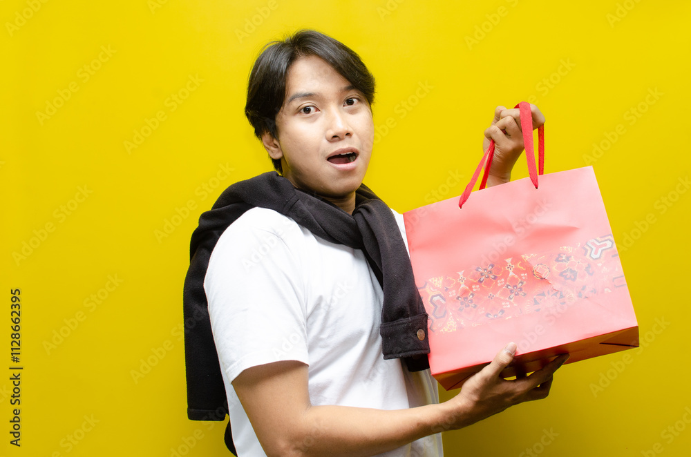 Fototapeta premium Side view of Happy Surprised Young Asian Man Holding Shopping Bags in Excitement