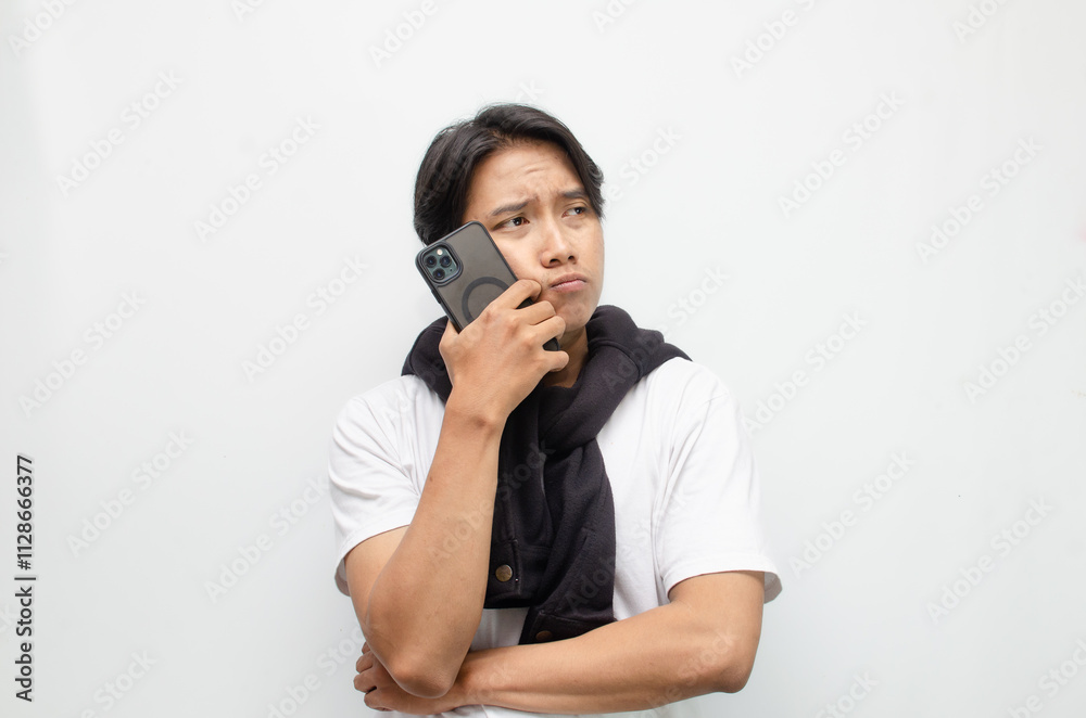 Sad and Pensive Young Asian Man Holding Smartphone with a Pouting Expression Sad and Pensive Young Asian Man Holding Smartphone with a Pouting Expression