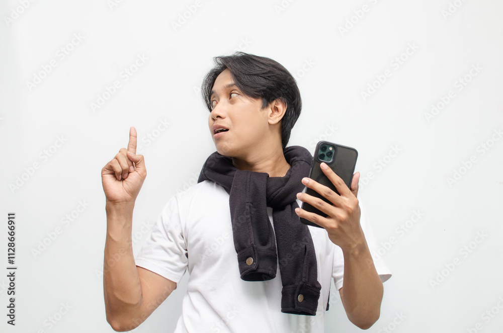 Excited Young Asian Man in Casual Outfit Holding Smartphone and Pointing with Joyful Expression Excited Young Asian Man in Casual Outfit Holding Smartphone and Pointing with Joyful Expression