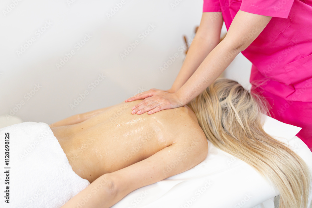 Obraz premium A therapist performing an oil massage on a woman's back in a serene spa setting. The session emphasizes relaxation, wellness, and self-care with a focus on professional treatment.