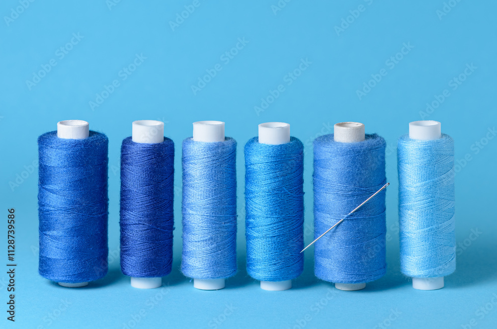 Row of blue thread spools with needle aligned background with copy space for text close-up flat lay top view Row of blue thread spools with needle aligned background with copy space for text close-up flat lay top view