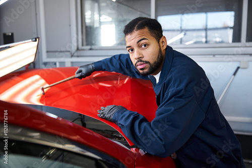 A young mechanic inspects a bright red car under the workshop lights, focused on his work. photo