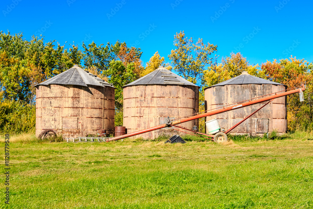 Three old grain silos sit in a field with a blue sky in the background Three old grain silos sit in a field with a blue sky in the background