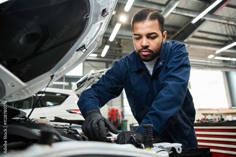 Handsome young mechanic works diligently under the hood of a vehicle in a busy garage. Handsome young mechanic works diligently under the hood of a vehicle in a busy garage.