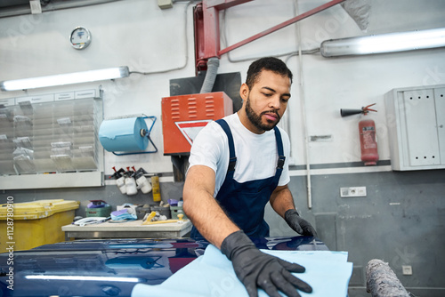 Passionate young mechanic works hard to restore a cars shine in a busy workshop environment. photo