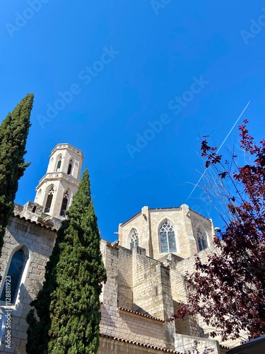 Saint Peter Church in Figueres with Tower and Cypress Trees Against Clear Blue Sky