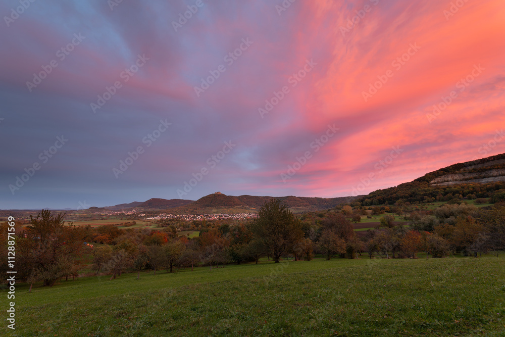 Obraz premium Blick auf die Burgfestung Hohenneuffen mit den drei Kaiserbergen am Horizont. Schwäbischen Alb im Herbst und einem gigantischen Sonnenuntergang.