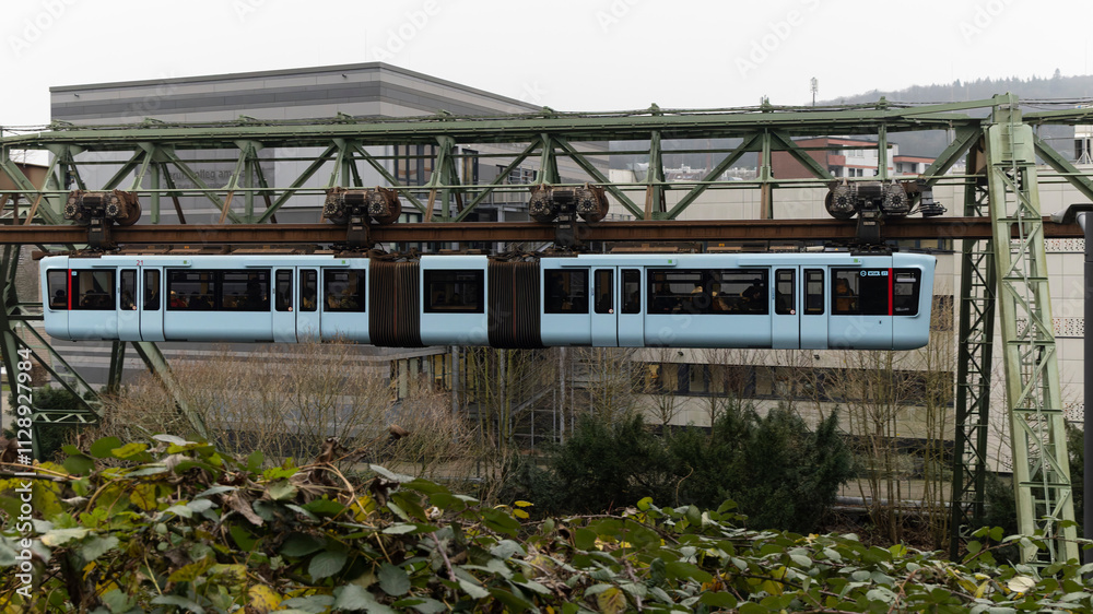 Obraz premium Ein blauer Schwebebahnwagen fährt über der Wupper vorbei