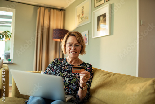 Smiling senior woman online shopping with credit card and laptop at home photo