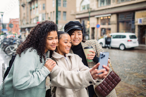 Young stylish female friends pointing while using phone for directions in the city photo