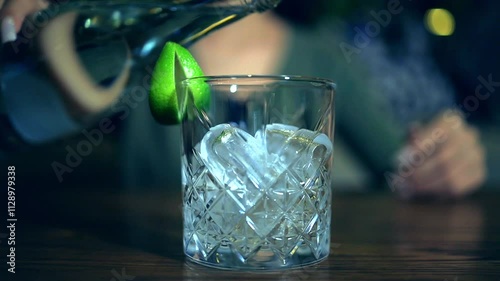 Close up of well-crafted cocktail served in a beautifully cut crystal glass, featuring ice cubes and a slice of lime. Clear non carbonated liquid poured into glass with ice cubes.