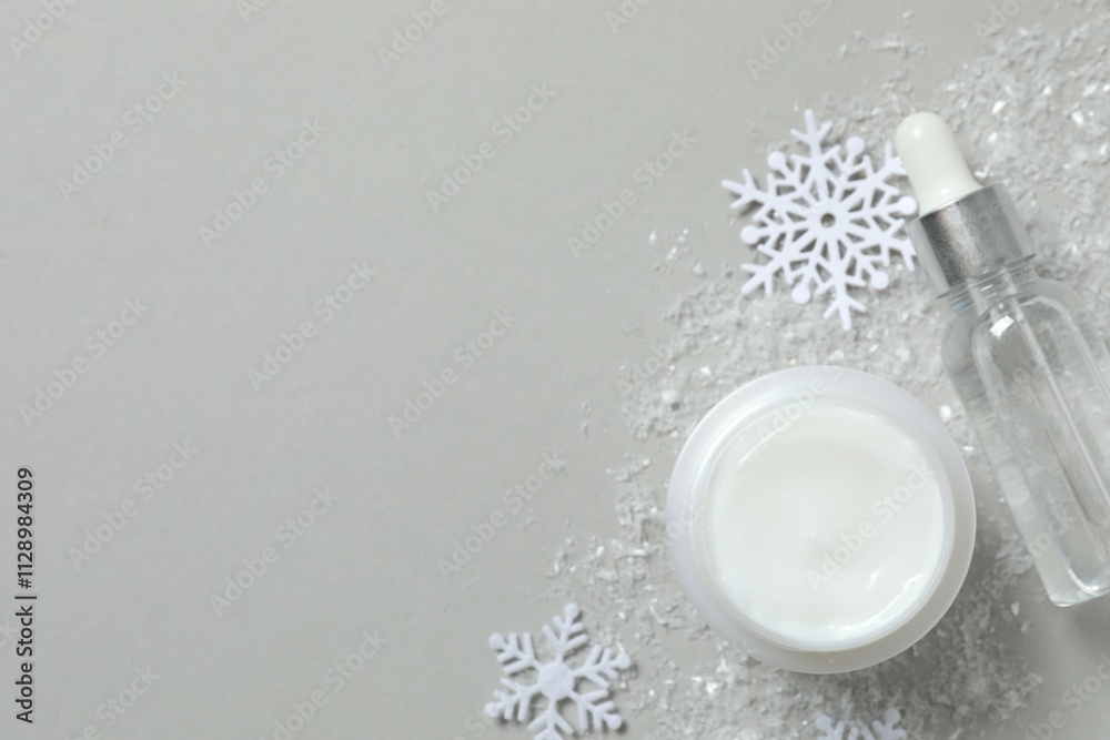 Fototapeta premium Winter skin care concept. Cosmetic products packaging design. Dropper bottle with serum, moisturizer cream jar and snowflakes on gray background. Flat lay, top view.
