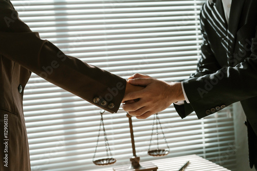 Two lawyers shaking hands in a law office with scales of justice in the foreground, symbolizing legal agreement and justice