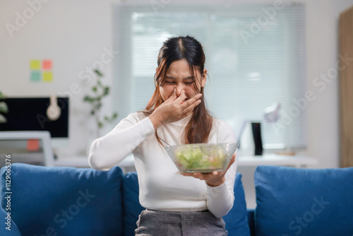 Young businesswoman is pinching her nose while holding a bowl of spoiled salad, showing a disgusted expression
