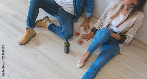 A man and woman are sitting on the floor with a bottle of wine between them