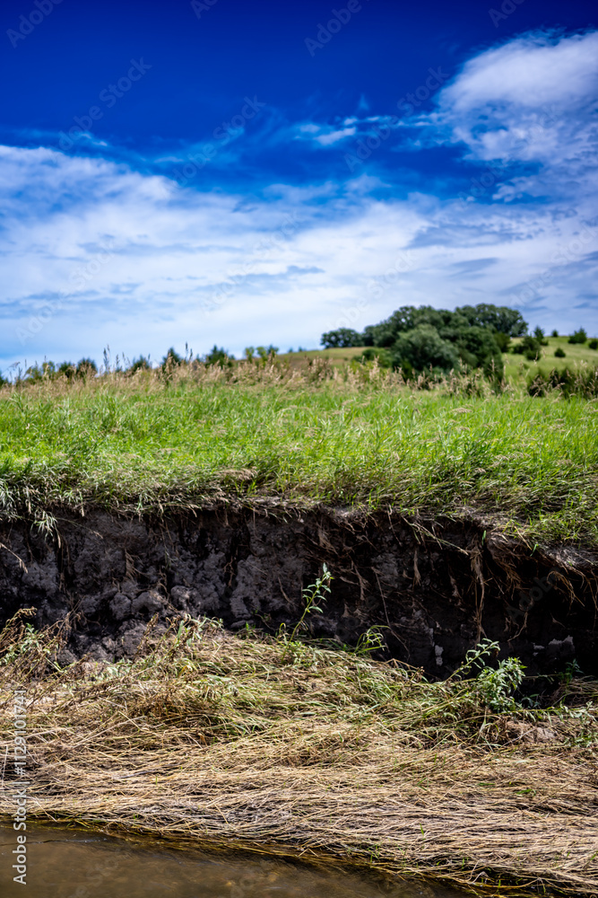 Soil erosion at drop off into a creek showing exposed roots and dirt along the water edge. Soil erosion at drop off into a creek showing exposed roots and dirt along the water edge.