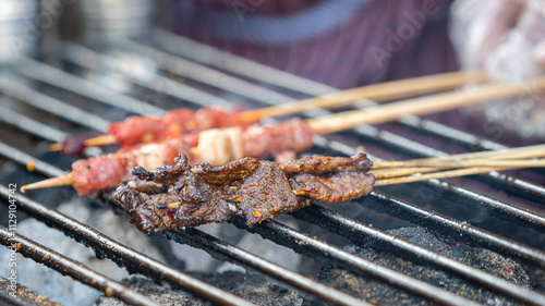 Beef meat on wooden skewer sticks are grilling on the metal grating with smoking from charcoal. Asian traditional streed food object, close-up. photo