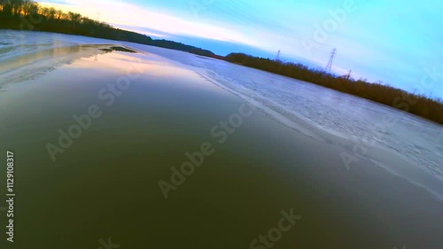 Colorful dawn sky reflected in the thin ice of a new day, moving aerial view.
