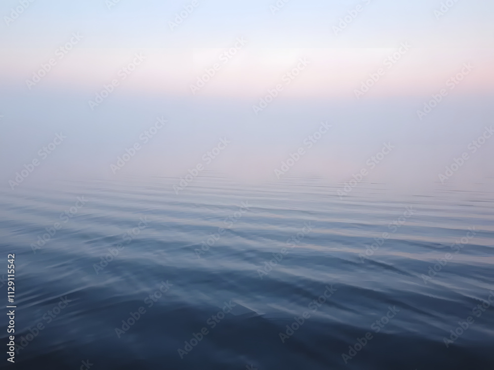 Fototapeta premium Gentle ripples on a calm lake at dawn, with fog and subtle pink and blue tones in the air