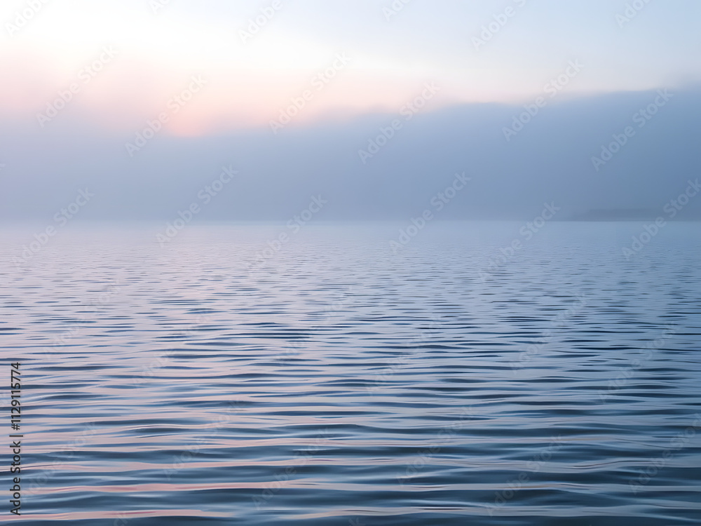 Obraz premium Gentle ripples on a calm lake at dawn, with fog and subtle pink and blue tones in the air