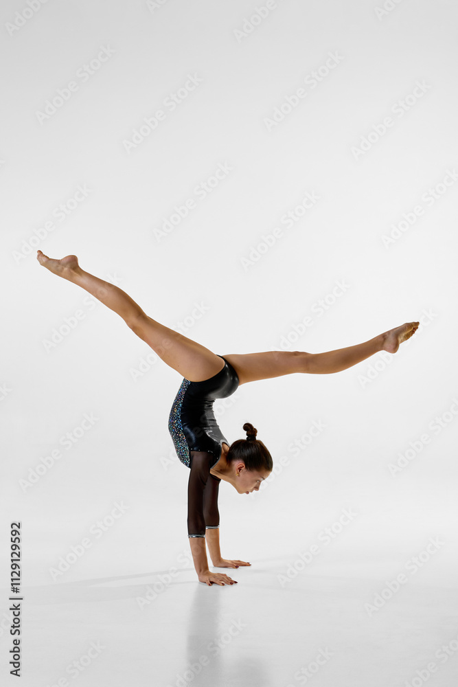 Gymnast performs steady movements, enhancing flexibility and posture, focus and control against white studio background. Copy space. Concept of professional sport, rhythm, elegance, movement. ad Gymnast performs steady movements, enhancing flexibility and posture, focus and control against white studio background. Copy space. Concept of professional sport, rhythm, elegance, movement. ad