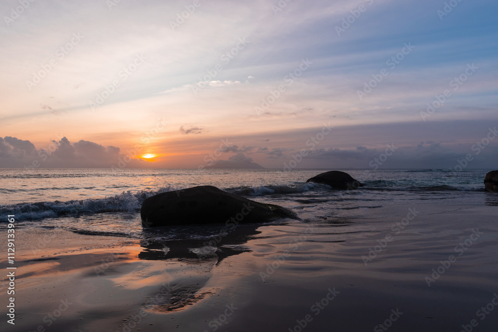 Naklejka premium Landscape with wet sand and silhouettes of dark coastal rocks
