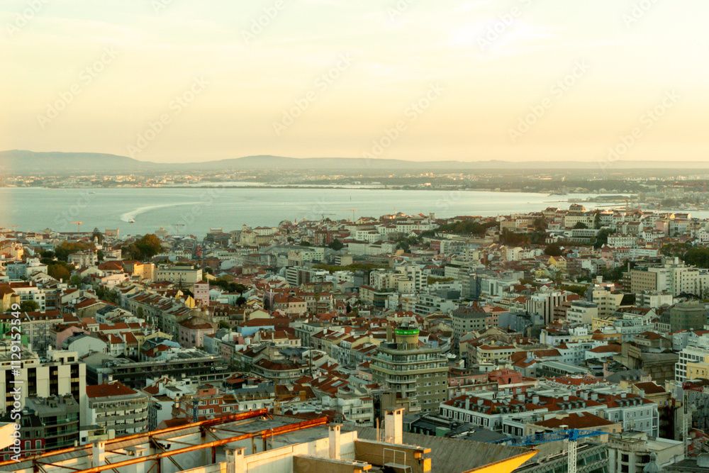 Naklejka premium Lisbon, Portugal - Rooftop view of the Tagus River and the rooftops of downtown Lisbon at golden hour with a ferry boat in the distance