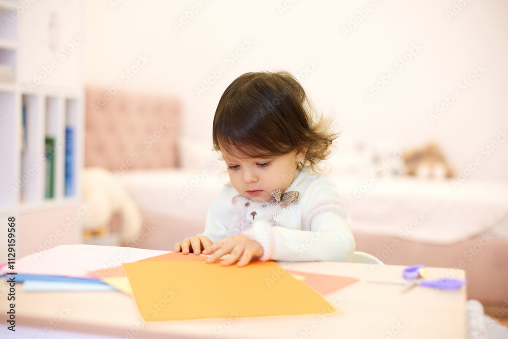 little child girl holding multi-color paper while sitting by table at home, Children creativity little child girl holding multi-color paper while sitting by table at home, Children creativity