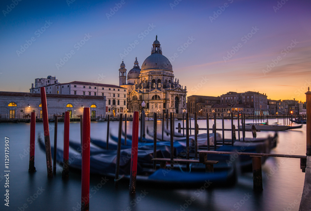 Naklejka premium Gondolas lined up by the Grand Canal at sunset in Venice with historic architecture in view
