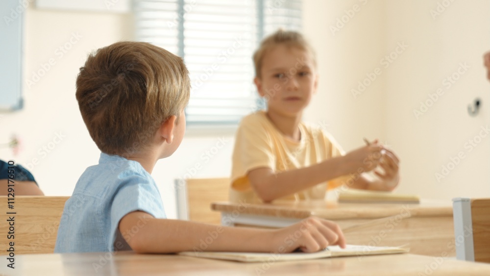 Beautiful teacher explaining test while caucasian boy doing classwork and listening explanation. Cute child looking at teacher while taking a notes or writing answer in paper at classroom. Pedagogy. Beautiful teacher explaining test while caucasian boy doing classwork and listening explanation. Cute child looking at teacher while taking a notes or writing answer in paper at classroom. Pedagogy.