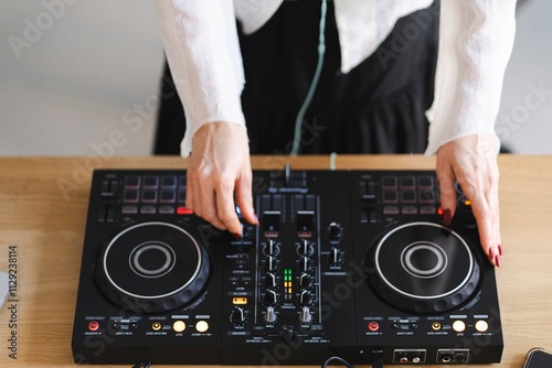 Close-up of a person’s hands with red painted nails adjusting knobs and sliders on a DJ controller photo