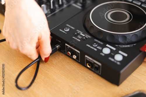 Close-up of a hand with red nails connecting a cable to a DJ controller photo