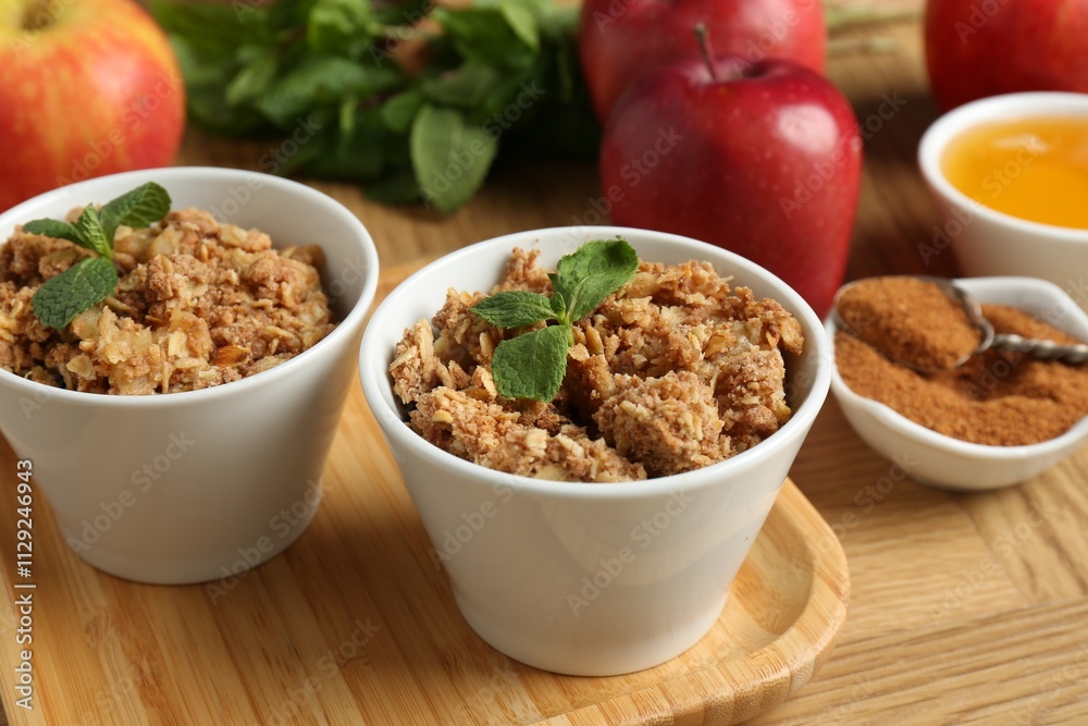 Delicious apple crisp in bowls, fresh fruits, cinnamon, mint and honey on wooden table, closeup Delicious apple crisp in bowls, fresh fruits, cinnamon, mint and honey on wooden table, closeup
