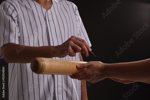 Baseball player signing autograph on bat against black background, closeup