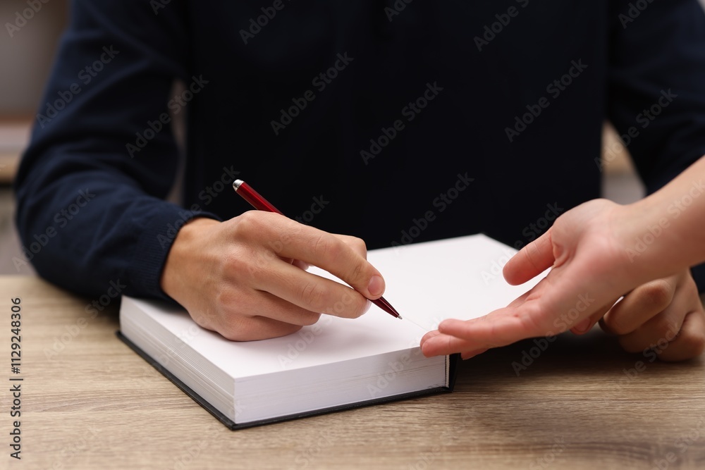 Obraz premium Writer signing autograph in book at wooden table indoors, closeup