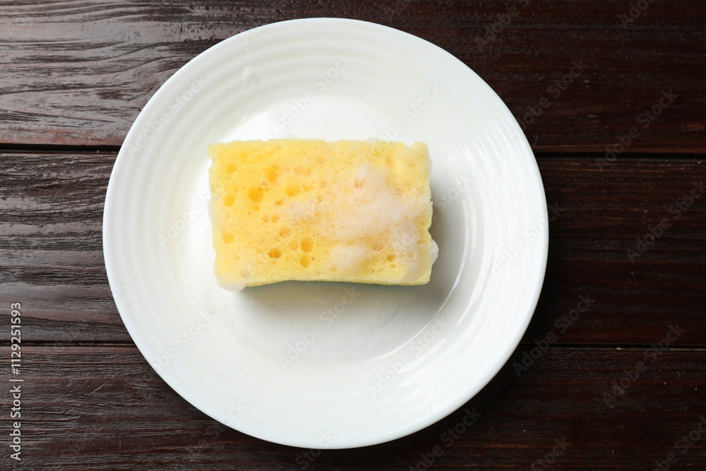 Yellow sponge with foam and plate on wooden table, top view Yellow sponge with foam and plate on wooden table, top view