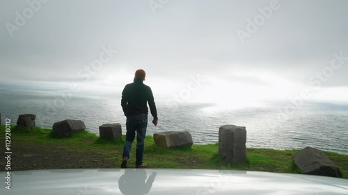 Man driver in hat walks to slope to enjoy seascape