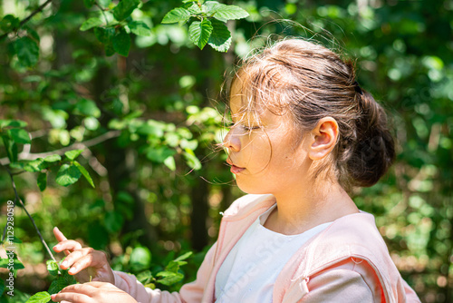 A young school girl in white and pink standing in lush green foliage
