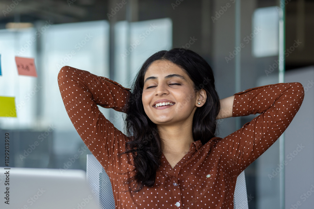 Smiling businesswoman leaning back at her workplace, embodying relaxation and contentment in a professional environment. Showcases a moment of satisfaction during work whilst embracing a balanced