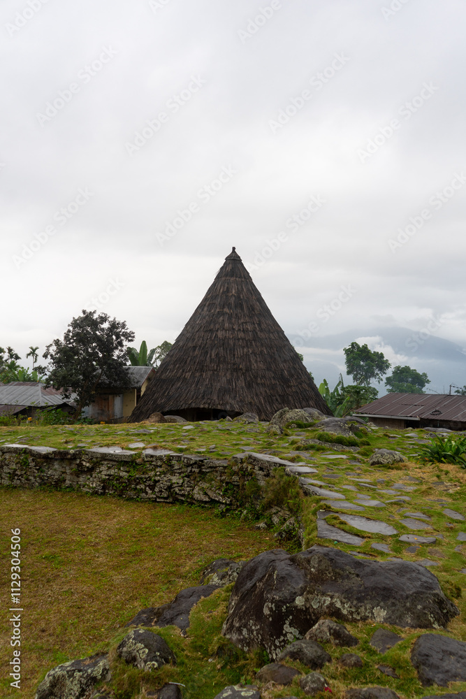 A traditional thatched-roof hut set against a misty, mountainous backdrop.