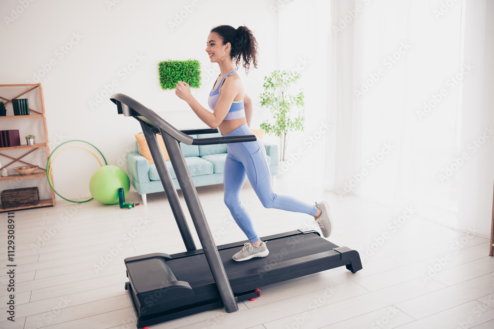 Fototapeta premium Energetic woman running on treadmill in bright modern home interior with natural light