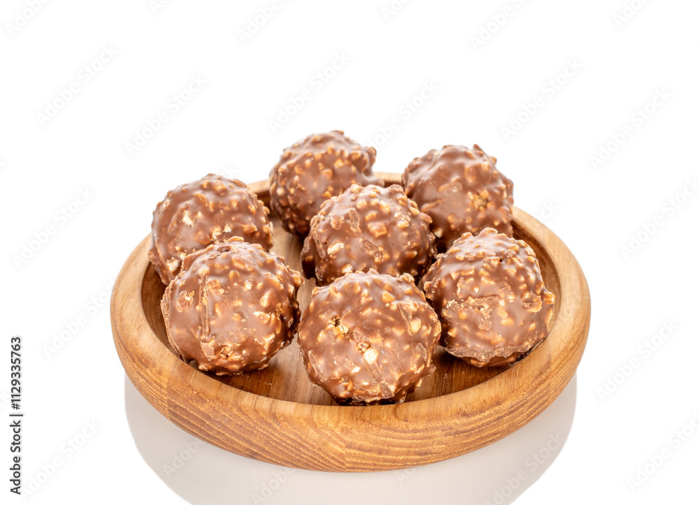Chocolate candies with hazelnuts in a wooden bowl, close-up, isolated on a white background. Chocolate candies with hazelnuts in a wooden bowl, close-up, isolated on a white background.