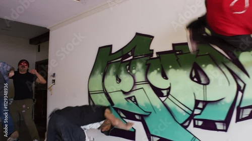 Two cool parkour artists do flips off a wall inside a house as their friends hype them up. photo