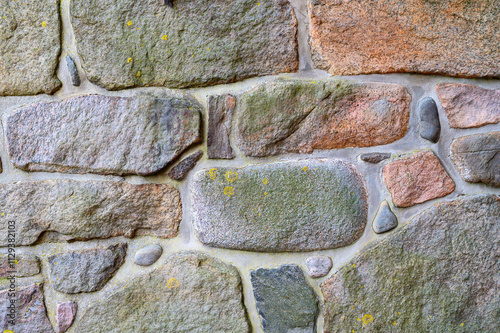 This rustic stone wall features a mix of different stone shapes and colors, highlighting natural textures and the interplay of light and shadow. Moss and lichens accentuate the surface photo