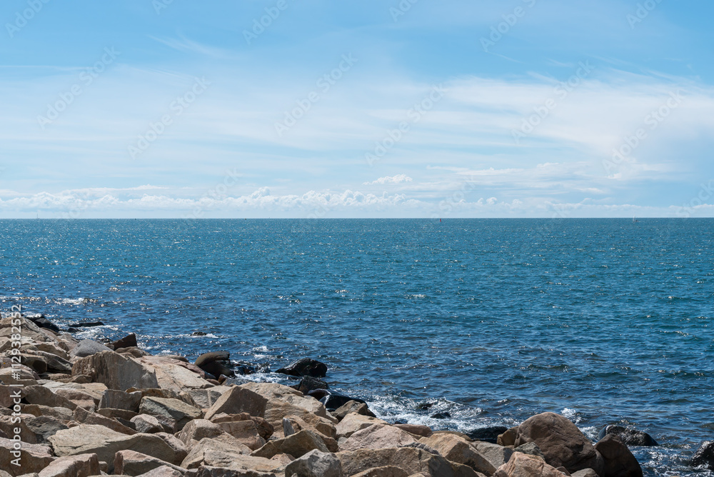 Gentle waves lap against a rocky shoreline under a bright blue sky. Soft clouds float above, creating a tranquil seaside atmosphere perfect for relaxation Gentle waves lap against a rocky shoreline under a bright blue sky. Soft clouds float above, creating a tranquil seaside atmosphere perfect for relaxation