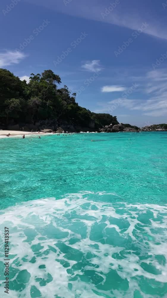 The tropical beach on Similan Islands in Thailand, has clear blue water, white sand, and lush green jungle under a sunny sky. The tropical beach on Similan Islands in Thailand, has clear blue water, white sand, and lush green jungle under a sunny sky.