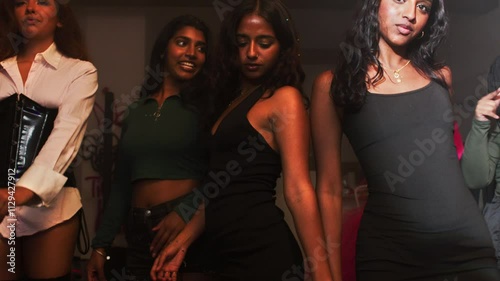 A group of young women dance in the middle of a house party as they look at the camera. photo